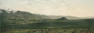Colorized photograph of green prairie with snow-capped mountains in the background.