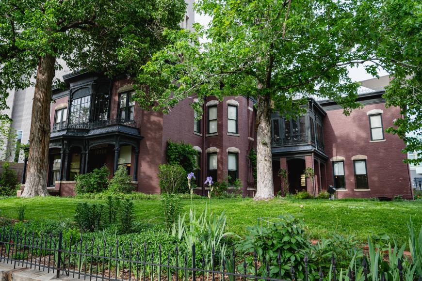 Exterior of the center for Colorado women's history. Lush green trees surround the old-fashioned, maroon brick exterior of the house.