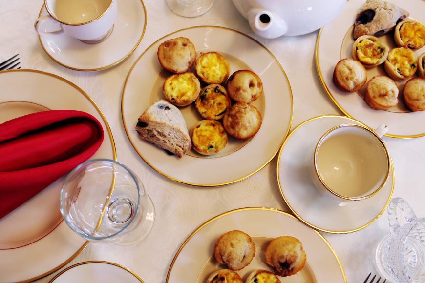 A table setting full of ceramic teacups and plates with a red napkin. There are scones and quiches displayed on the plates.