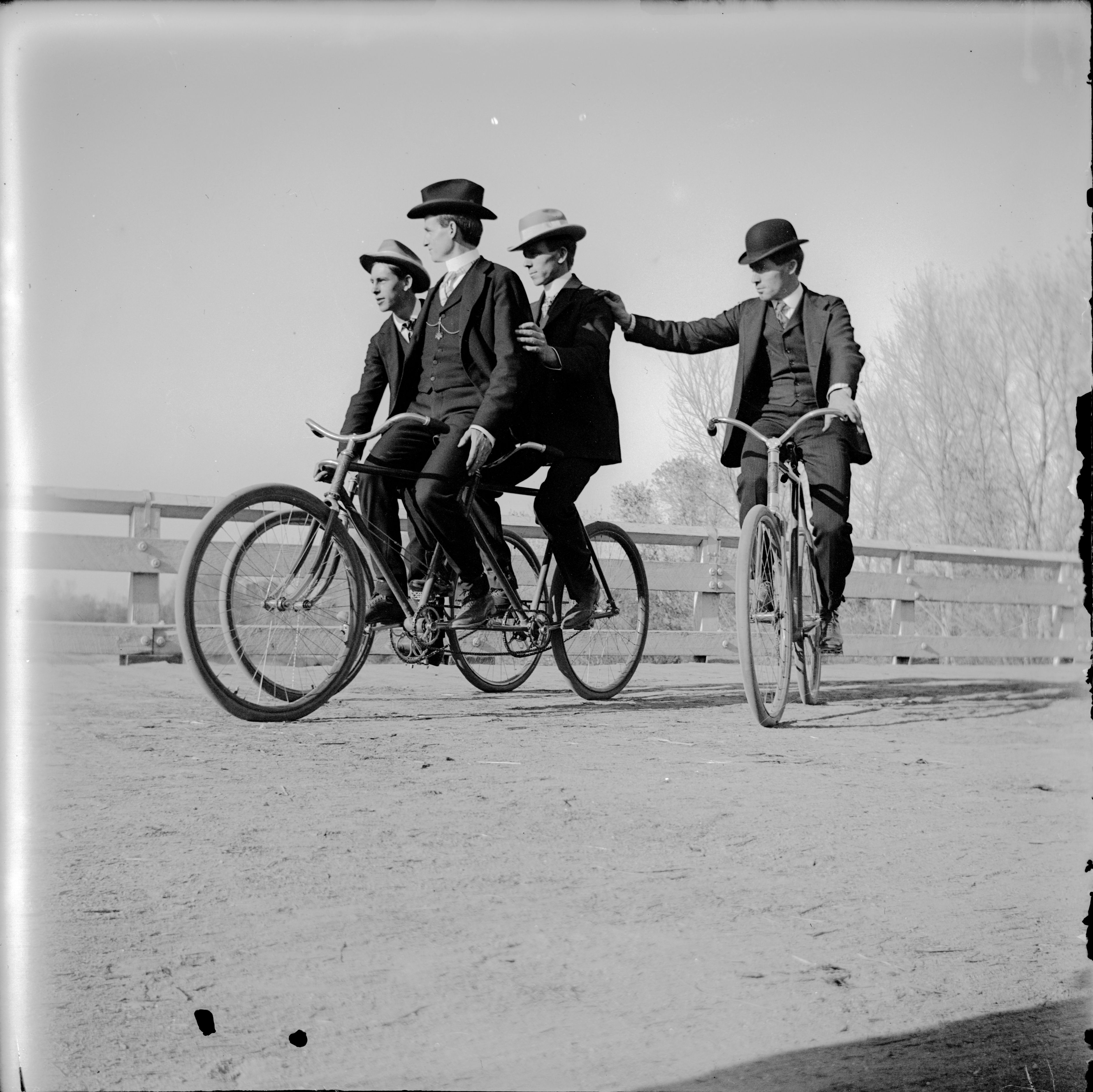 A group of men ride bicycles, including one tandem bike, over Alameda Avenue Bridge in Denver, 1904-09