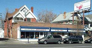 A triple-storefront addition of mid-twentieth century vintage fills multiple lots in front of a Queen Anne style house.