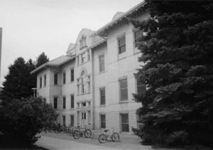 A blacka nd white photo of the building from an angle with evergreens on either end of the photo.