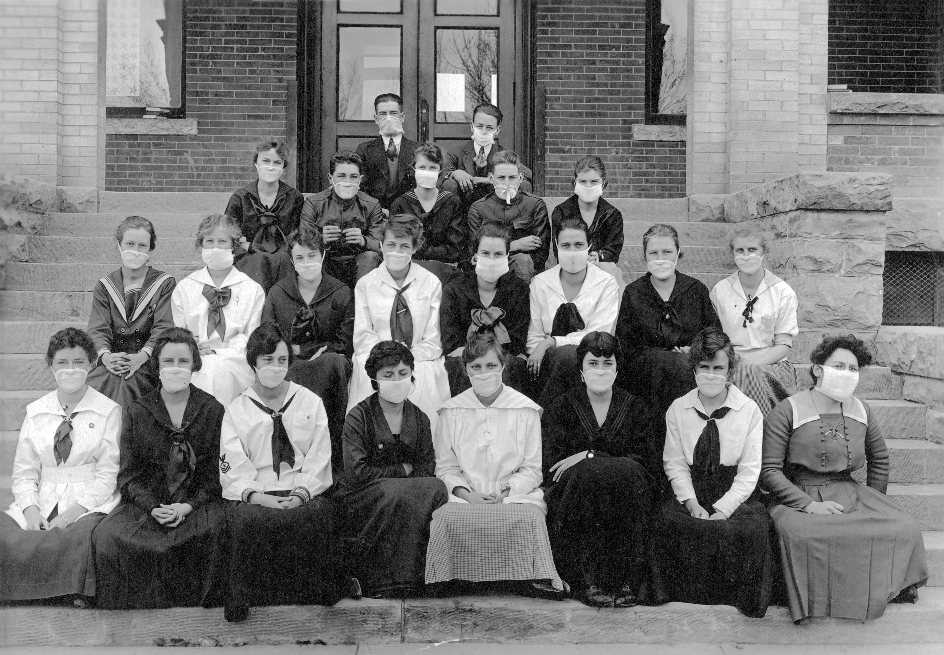 Photo taken in 1918. Twenty-three high school students sit on the front steps of their school in Canyon City, Colorado for a formal group picture. This is during the Influenza pandemic of 1918-1919, so every student is wearing mask covering their noses and mouths as protection from the flu.