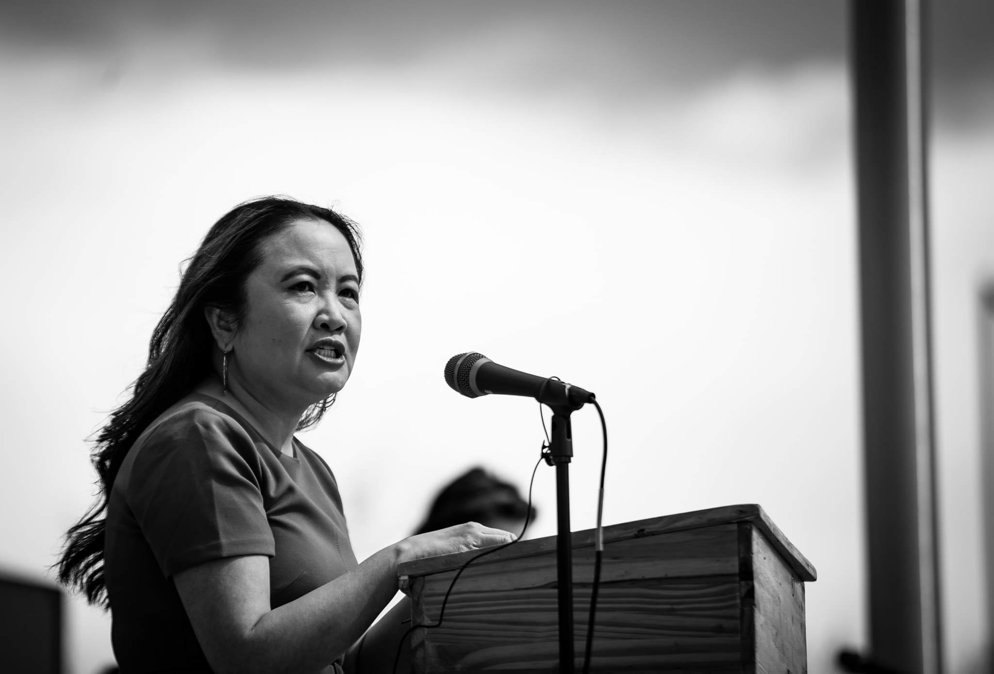 Photo of Nga Vương-Sandoval standing at a podium, speaking into a microphone.