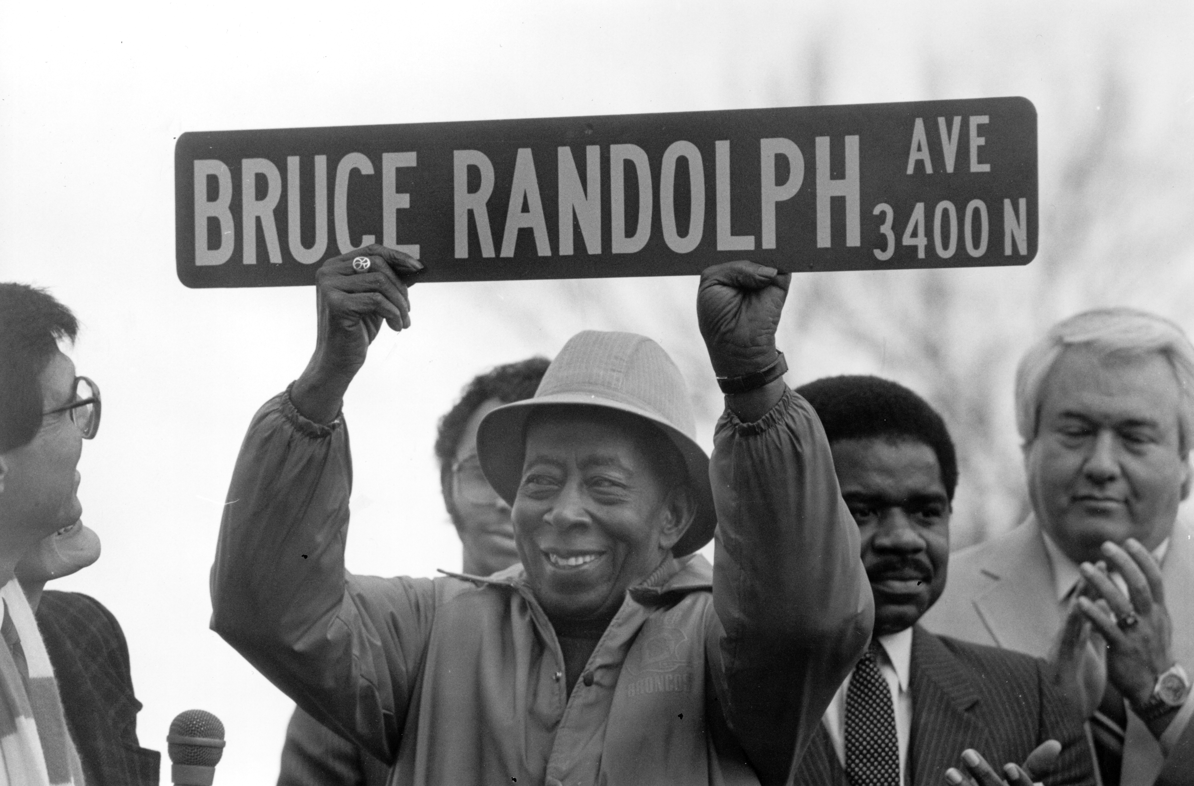 Bruce Randolph holding up a street sign which reads: "Bruce Randolph, Ave."