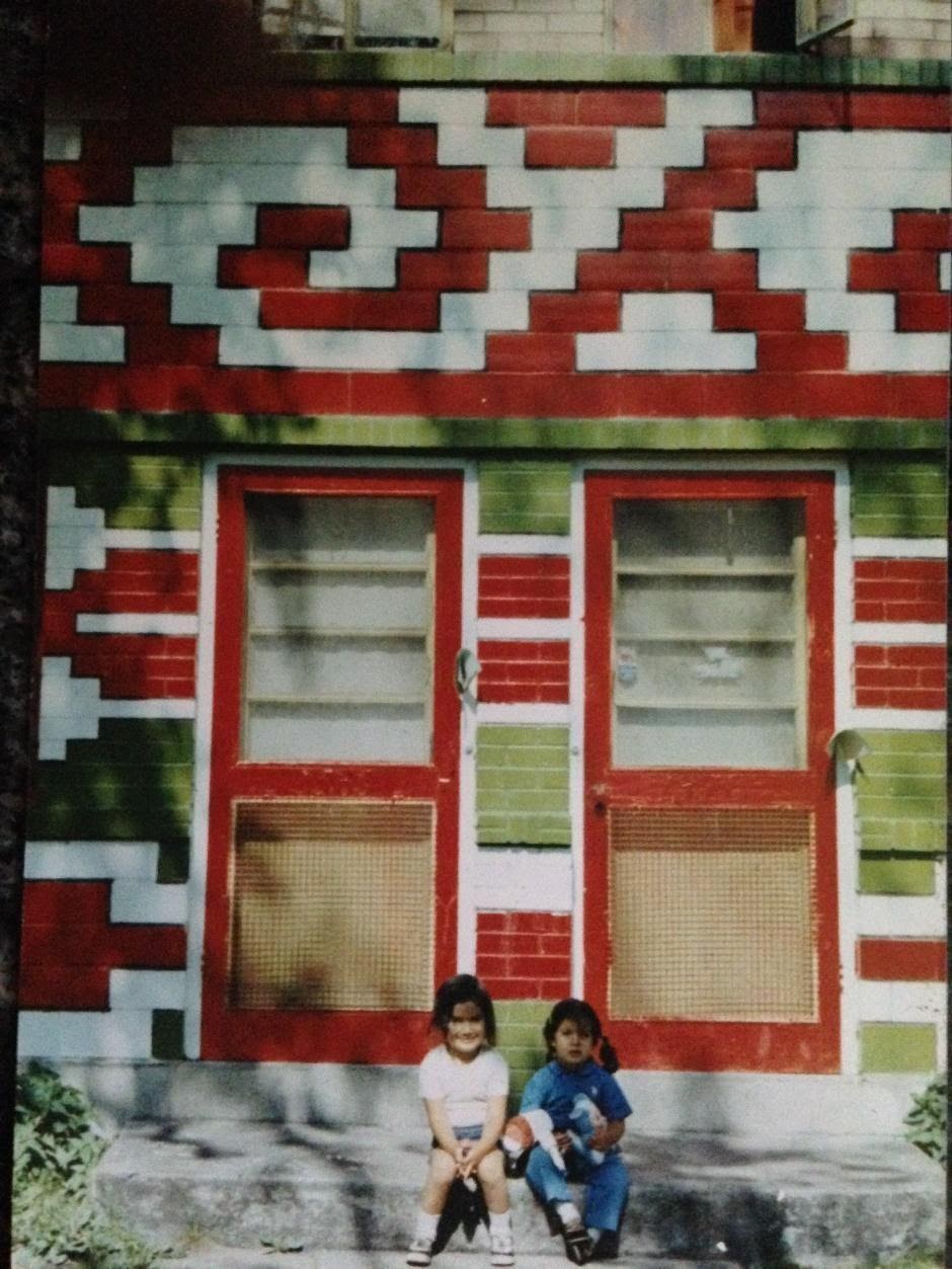 A colorful geometric mural in red, white, and green adorns the front of a residential building with two doors.