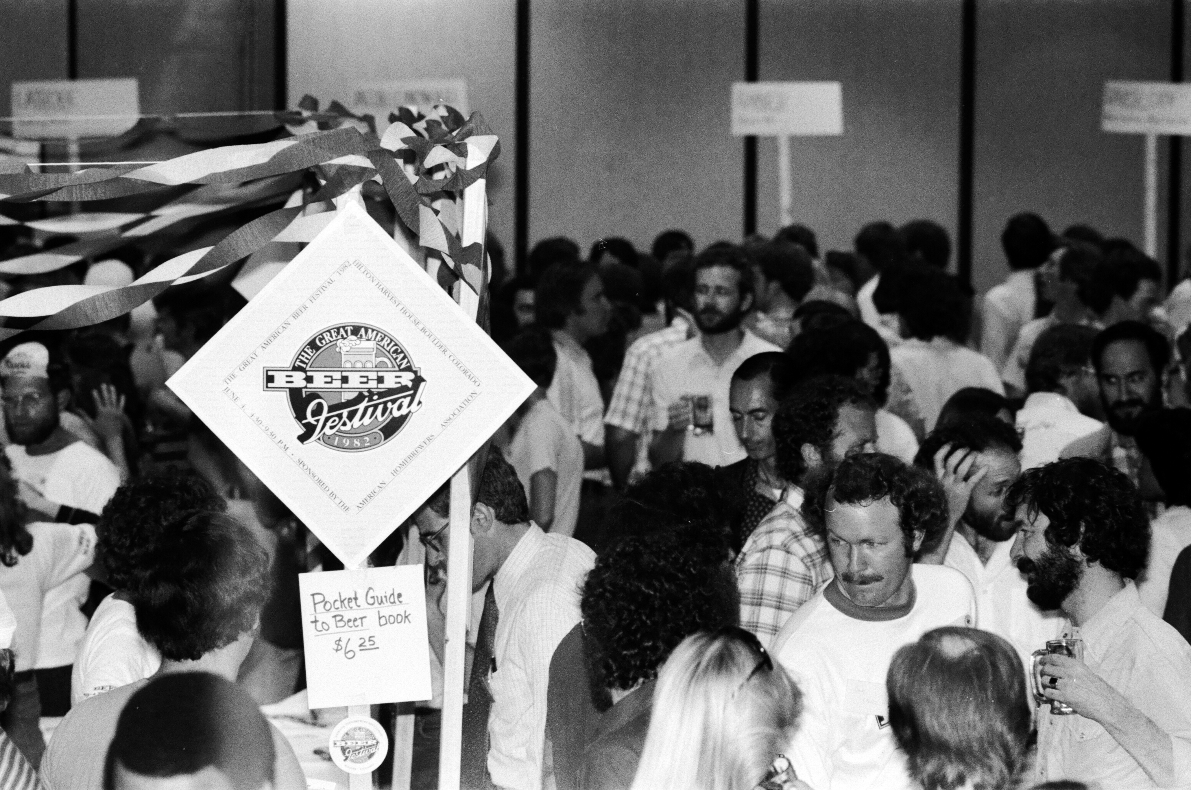 A crowd of people in a building. Above them hangs a sign reading "The Great American Beer Festival, 1982."