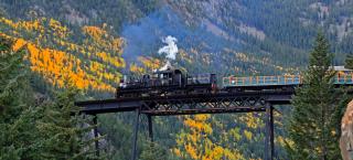 The Georgetown Loop train crosses a bridge. Fall is changing the aspens yellow and green in the background.
