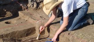 Person excavating remains of a wooden feature.