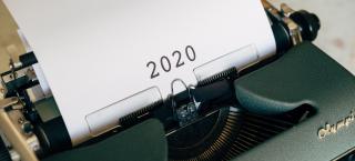 Photo of an old Olympic typewriter, with a piece of white typing paper in it, which simply says "2020" in large black numerals.