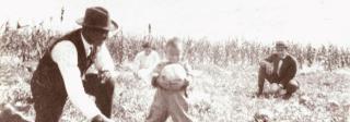 A Black family, including two adult men and a small child kneel in a field. The child holds a large vegetable and is smiling for the camera.