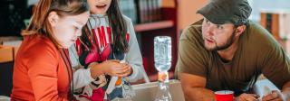 Two students work on an experiment with a teacher at a table at Hands-On History