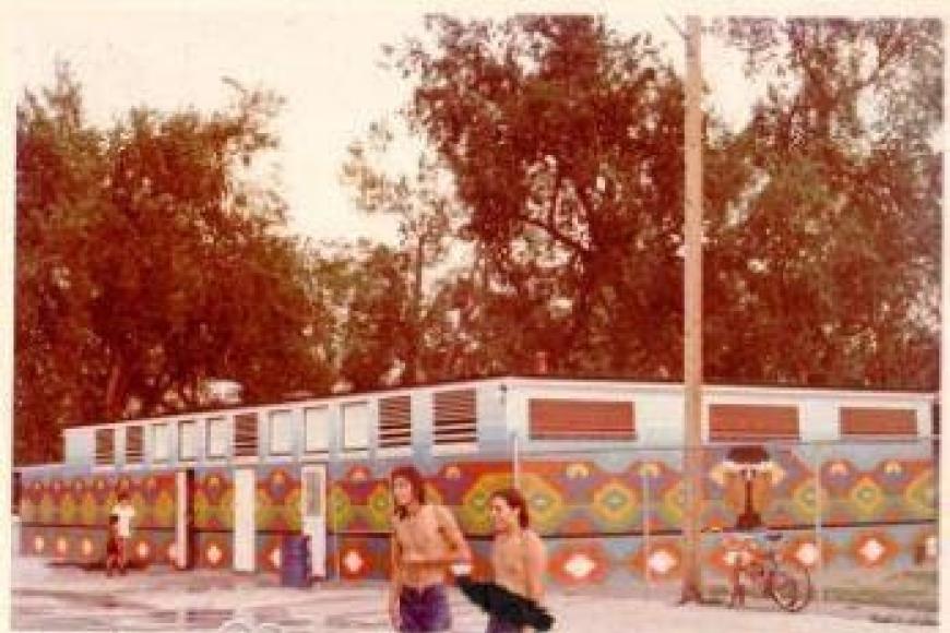 A colorful, geometric mural on the side of a pool building. The photo is visibly aged and the color has faded.