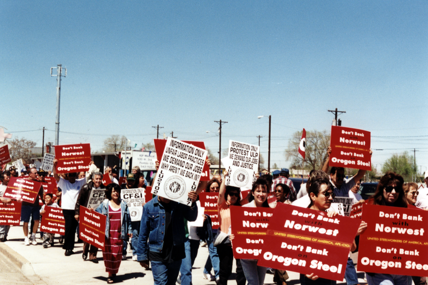 A group of marching protestors in Pueblo. They hold sides reading "Don't Bank with Northwest. Don't Bank on Oregon Steel."