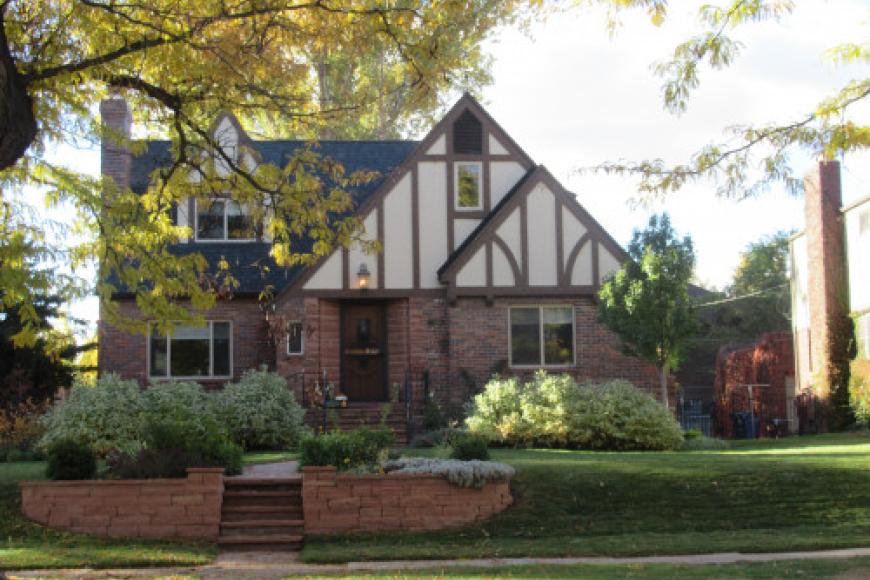 A tudor style home slightly obscured by greenery.
