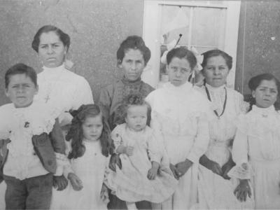 An historic photo of two women sitting amongst one boy and five girls, all ranging in ages from about one year old to teens.
