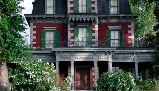 Front shot of Bloom House , including stone stairway with railing, and green window shutters and red paneling.