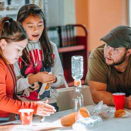 Two students work on an experiment with a teacher at a table at Hands-On History